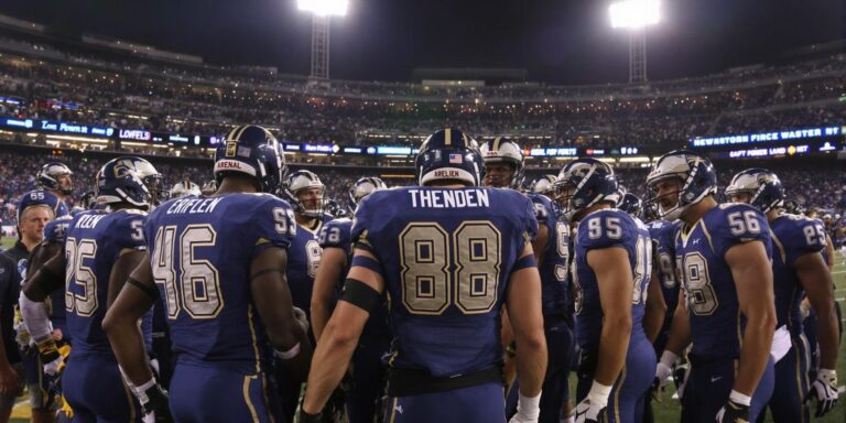 Arena Football League players huddle on lit stadium field