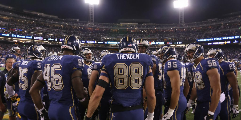 Arena Football League players huddle on lit stadium field