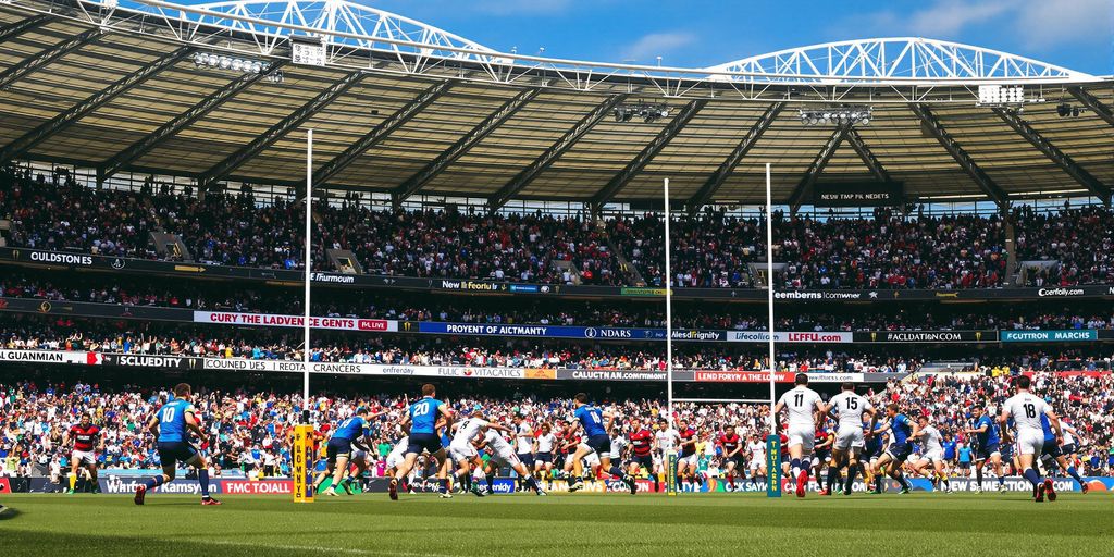 Rugby players tackling on field with cheering stadium crowd
