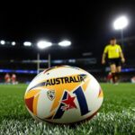 AFL ball on grass with referee and players behind