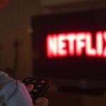 Smiling person with remote watching Netflix logo on television