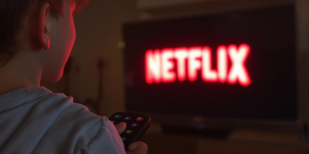 Smiling person with remote watching Netflix logo on television