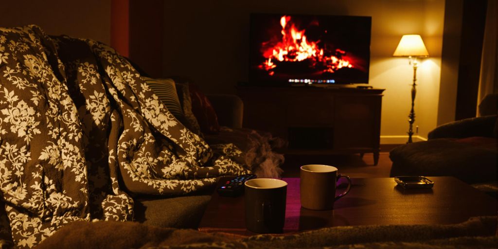 Cosy living room with sofa, blankets, remote and glowing TV